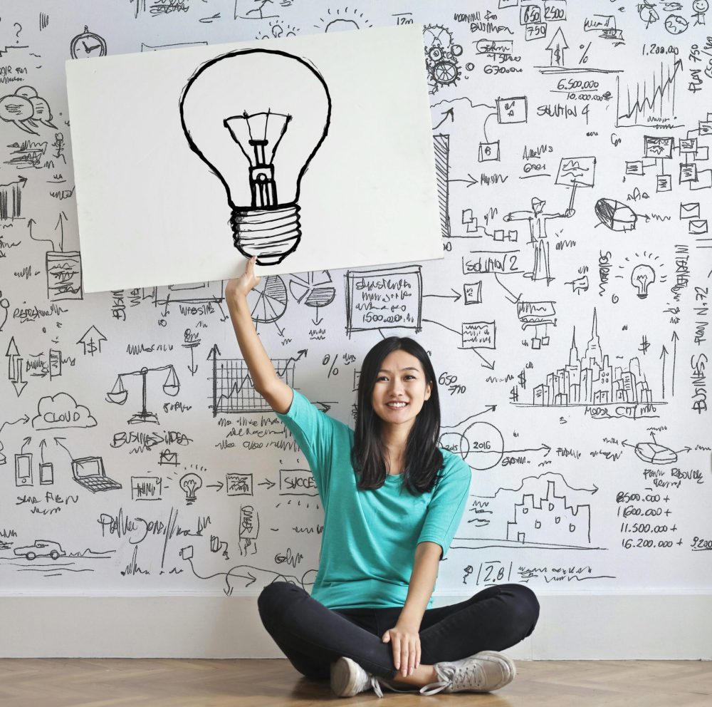 Young woman holds a light bulb drawing against a creative brainstorming wall.